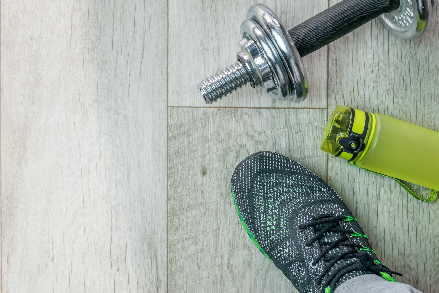 Green water bottle, dumbbell and training shoe on a light wood floor