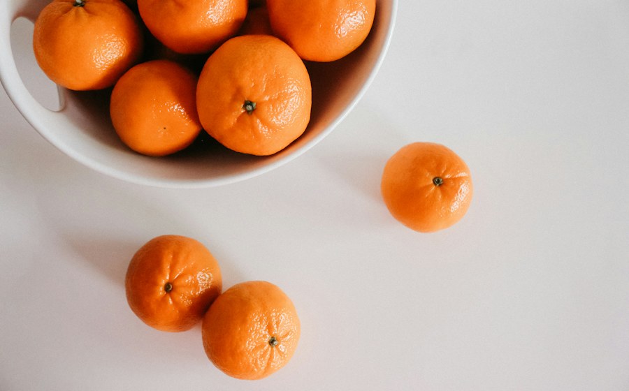 Fresh oranges in a white bowl on a light surface
